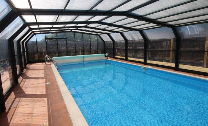 Photo of the heated swimming pool at Ysgubor Degwm on the Llyn peninsula. Swimming pool with blue tile liner with a retractable roof and terracotta ti